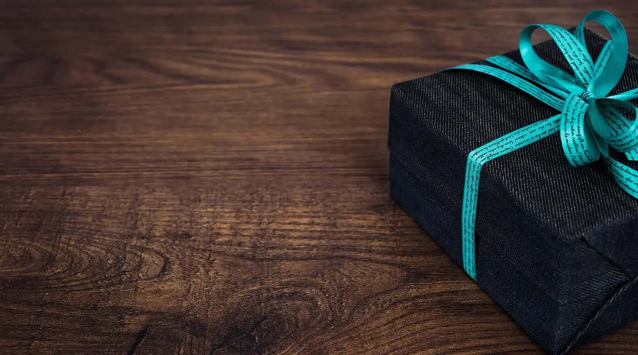 A dark wrapped gift box tied with a teal ribbon on a wooden table