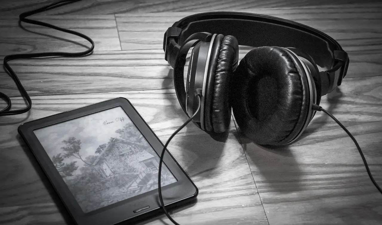 An e-reader and a pair of headphones on a wooden floor