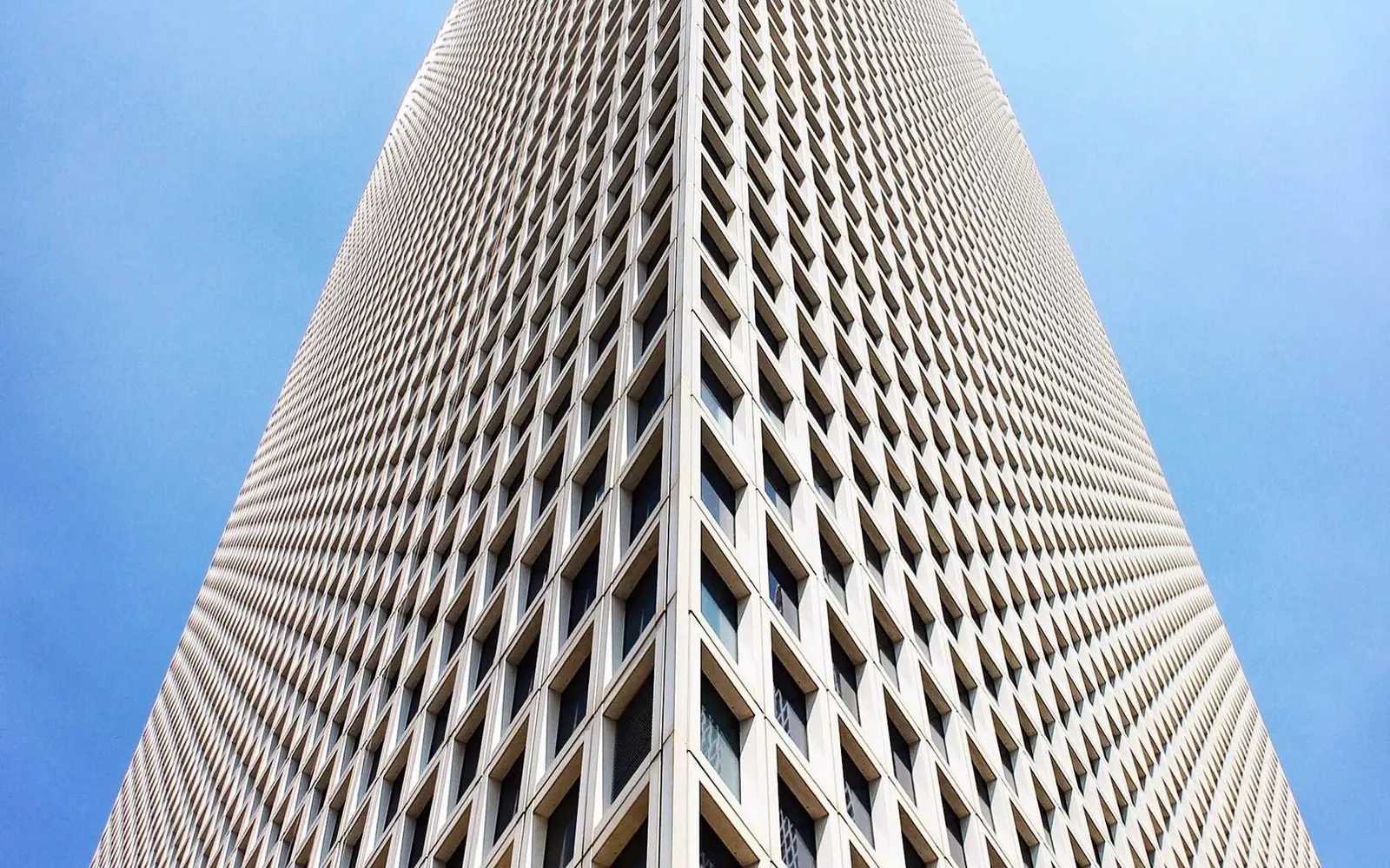 Tall white building facade seen from below against a blue sky