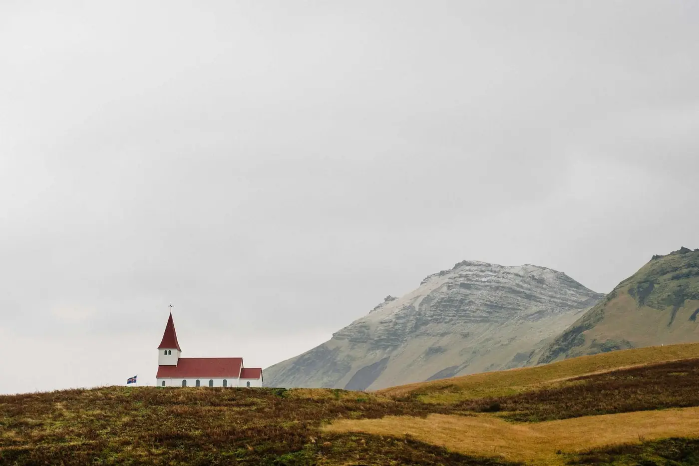Small white church with a red roof in green hills