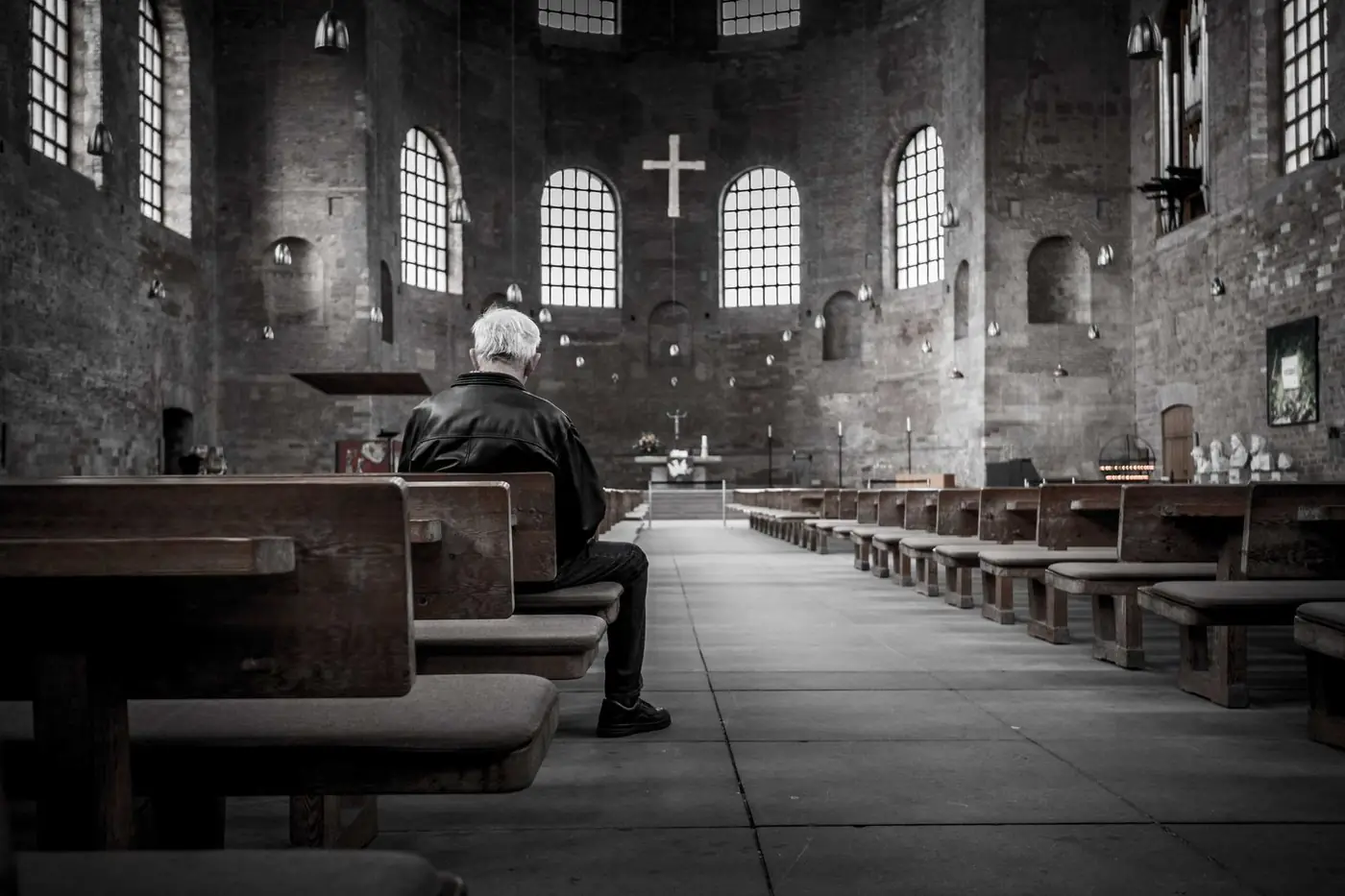 A person seated alone in a pew, facing the altar of a stone cathedral