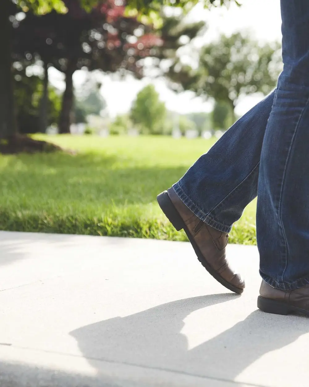 Person in jeans and shoes walking across a park